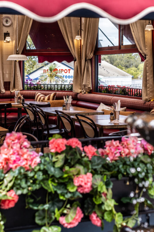 Cozy and vibrant outdoor dining area at Mezza Eatery in Forster, featuring stylish decor with patterned flooring, red accents, comfortable seating, and large windows offering a bright and inviting atmosphere.