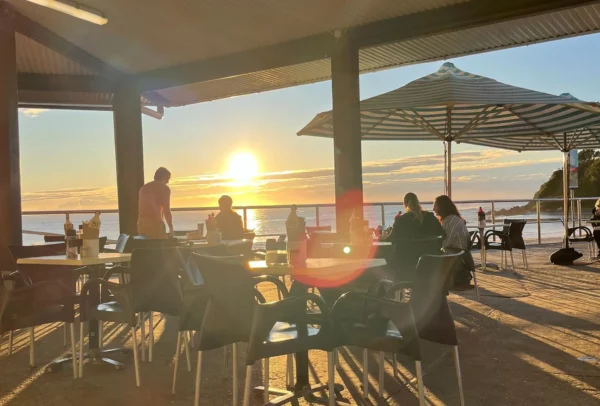 Sunset dining at Beach Bums Café on Forster Main Beach, featuring outdoor seating with stunning ocean views, creating a serene and picturesque atmosphere.